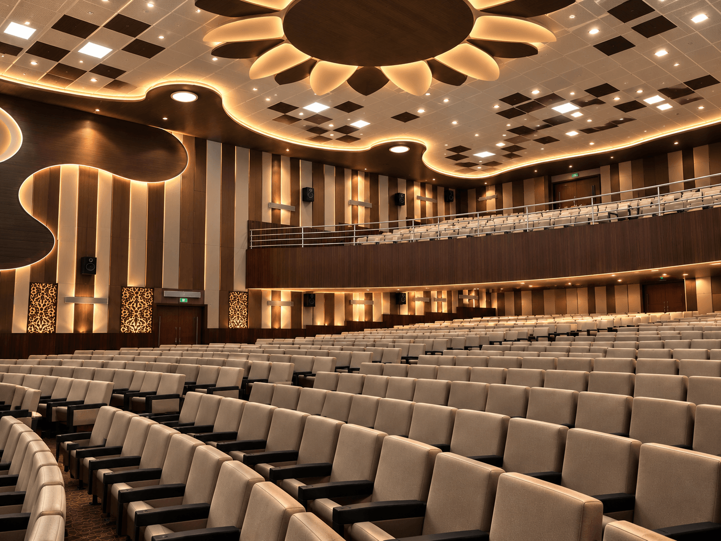 Design visualisation of a modern auditorium with sculpted dark timber ceiling forms, warm integrated lighting, a balcony and cream tiered seating