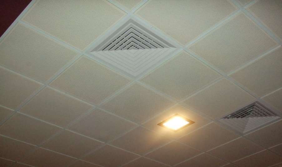 Installed perforated metallic false ceiling tiles with square air-conditioning diffusers and a recessed light